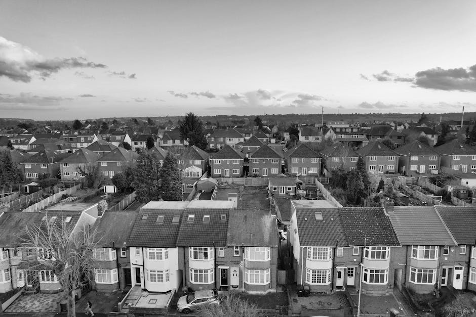 A black and white aerial photograph of a residential neighbourhood showing a row of terraced houses with bay windows and sloped tiled roofs. In the foreground, a man from Man with Van Wimbledon is eng