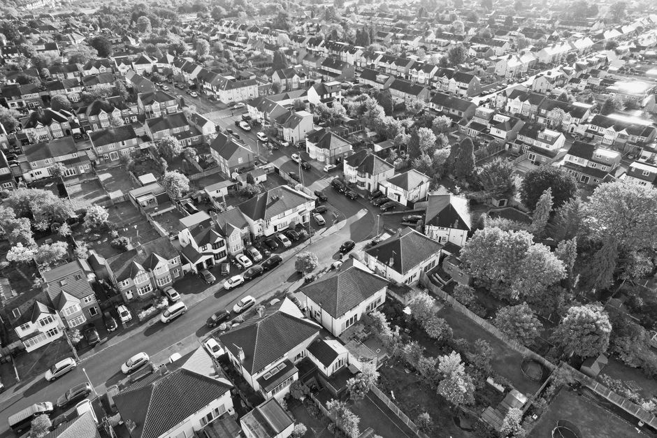 A black and white aerial photograph of a residential neighbourhood showing a row of terraced houses with bay windows and sloped tiled roofs. In the foreground, a man from Man with Van Wimbledon is eng